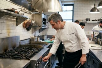 Chef professionnel inspectant une cuisinière commerciale en acier inoxydable dans une cuisine de restaurant
