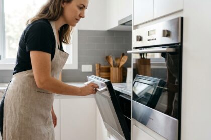 Femme ouvrant un four encastrable intégré dans une cuisine moderne aux meubles blancs et plan de travail en marbre